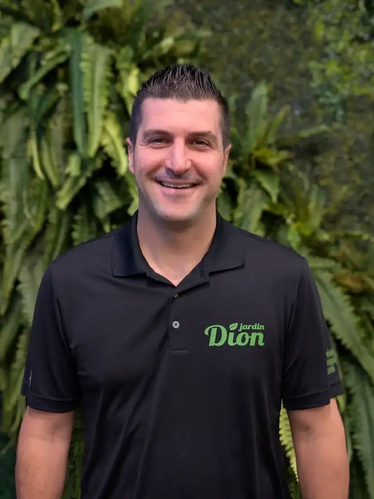 Homme souriant portant un polo Jardin Dion dans un jardin luxuriant.