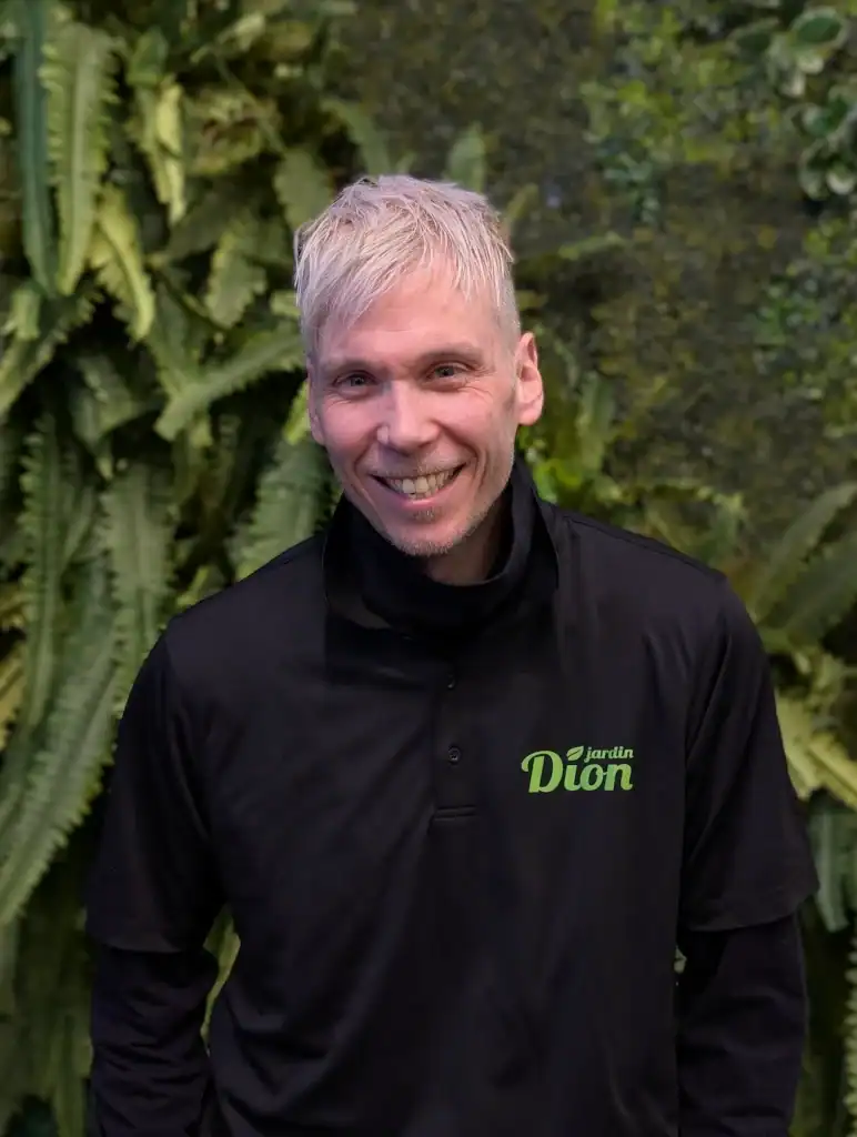 Employé de Jardin Dion souriant dans un jardin luxuriant.