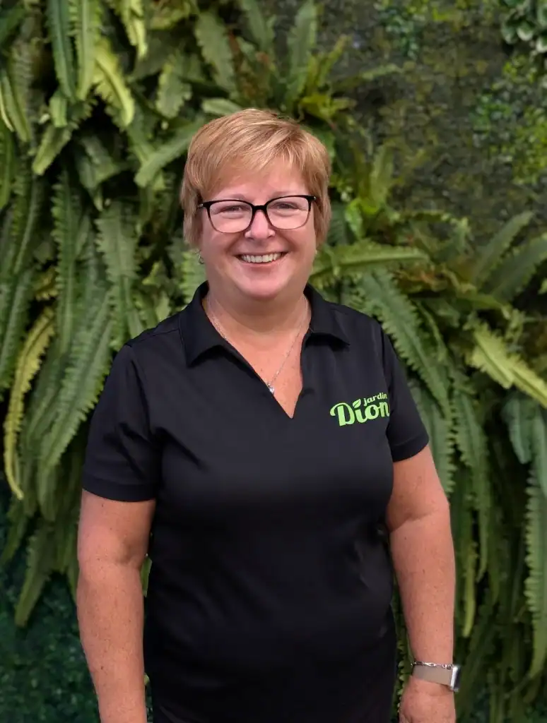 Femme souriante portant un polo Jardin Dion devant une végétation luxuriante.
